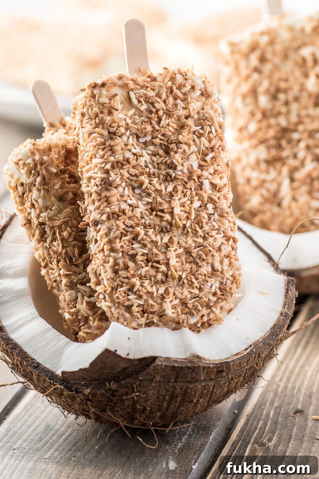 Toasted coconut cream popsicles displayed inside of a cracked fresh coconut
