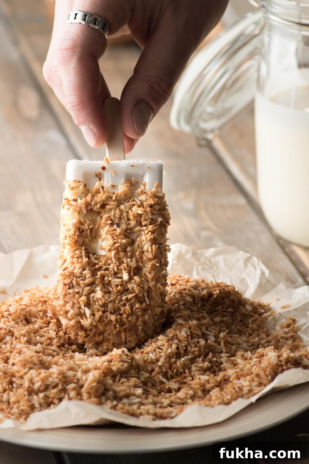 white coconut popsicles dipped in white chocolate being coated in toasted coconut 