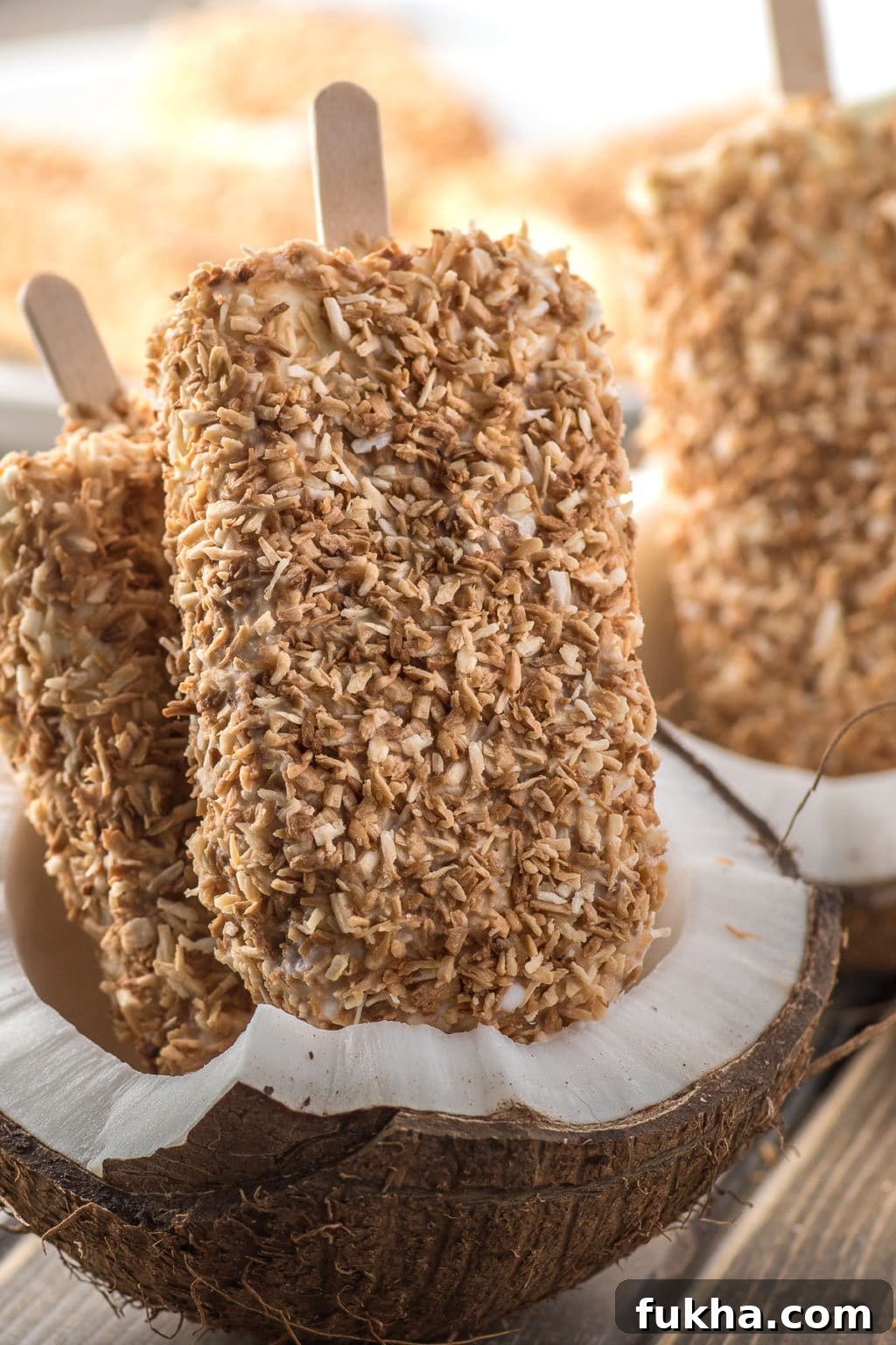 Toasted coconut cream popsicles displayed inside of a cracked fresh coconut