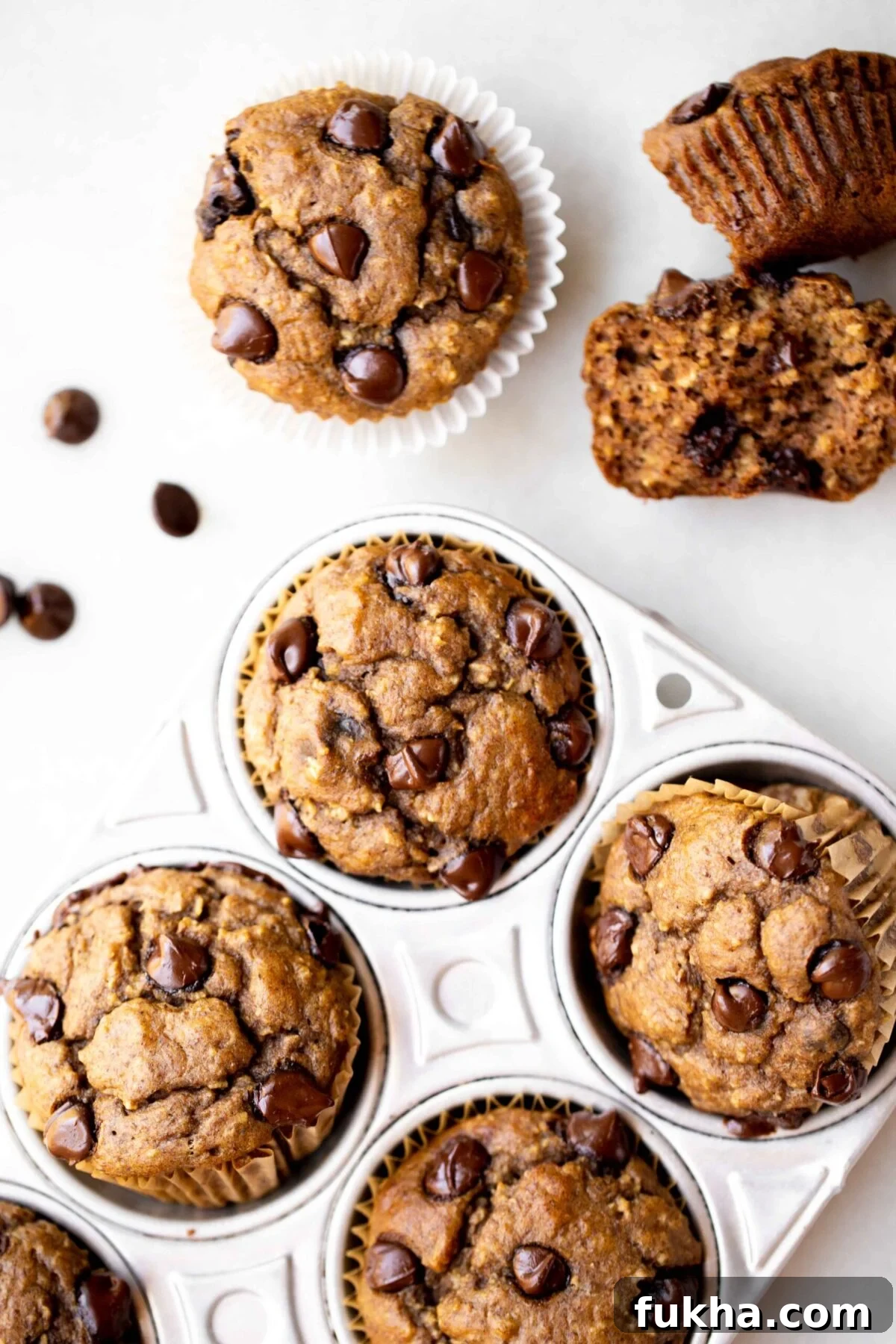 overhead photo of freshly baked healthy muffins, chocolate chip banana muffins, in an aluminum muffin pan with milk and chocolate chips in the background