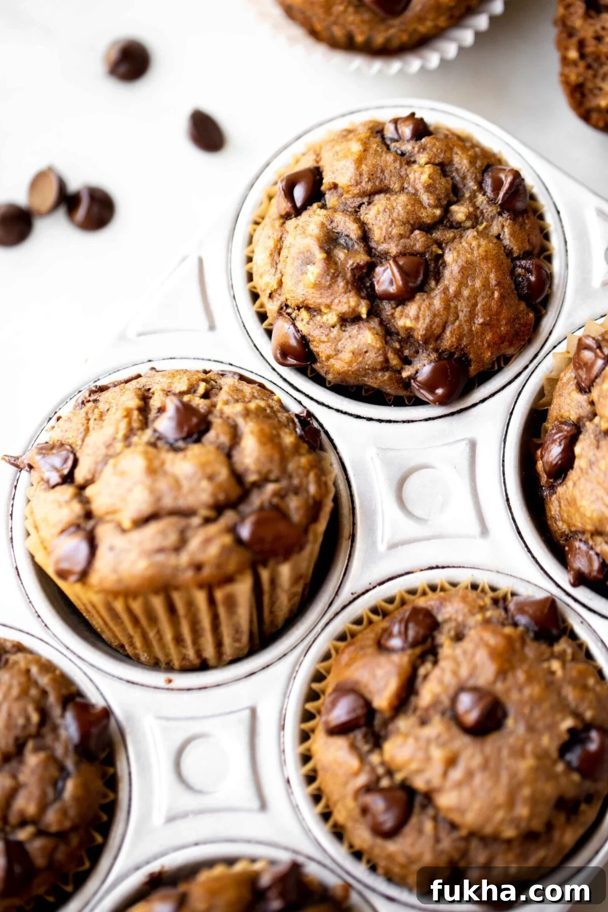 closeup photo at 45 degree angle of freshly baked chocolate chip banana muffins in an aluminum muffin pan on a light gray marble background