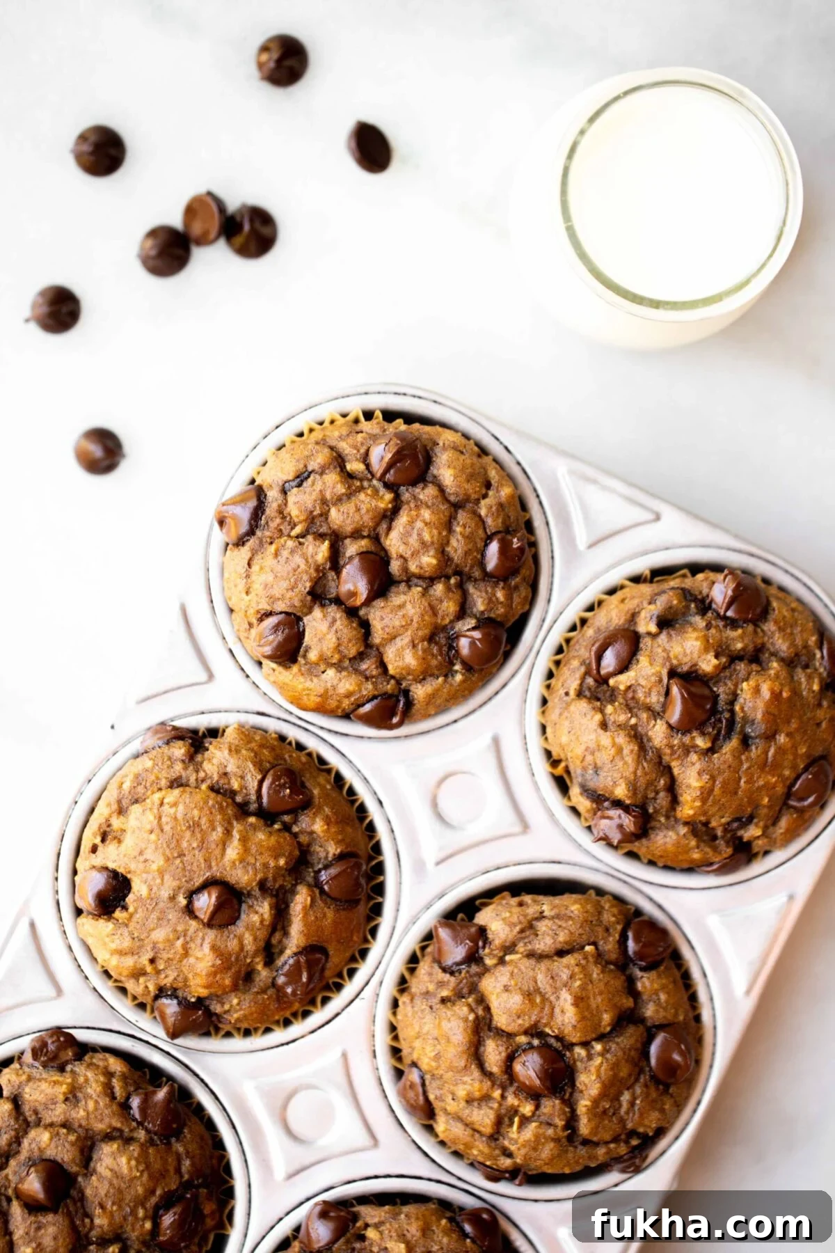 overhead photo of freshly baked chocolate chip banana muffins in an aluminum muffin pan with milk and chocolate chips in the background