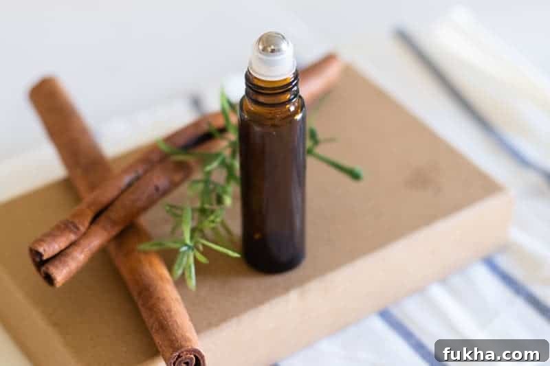 Amber roller bottle standing on box with cinnamon sticks and rosemary behind it.
