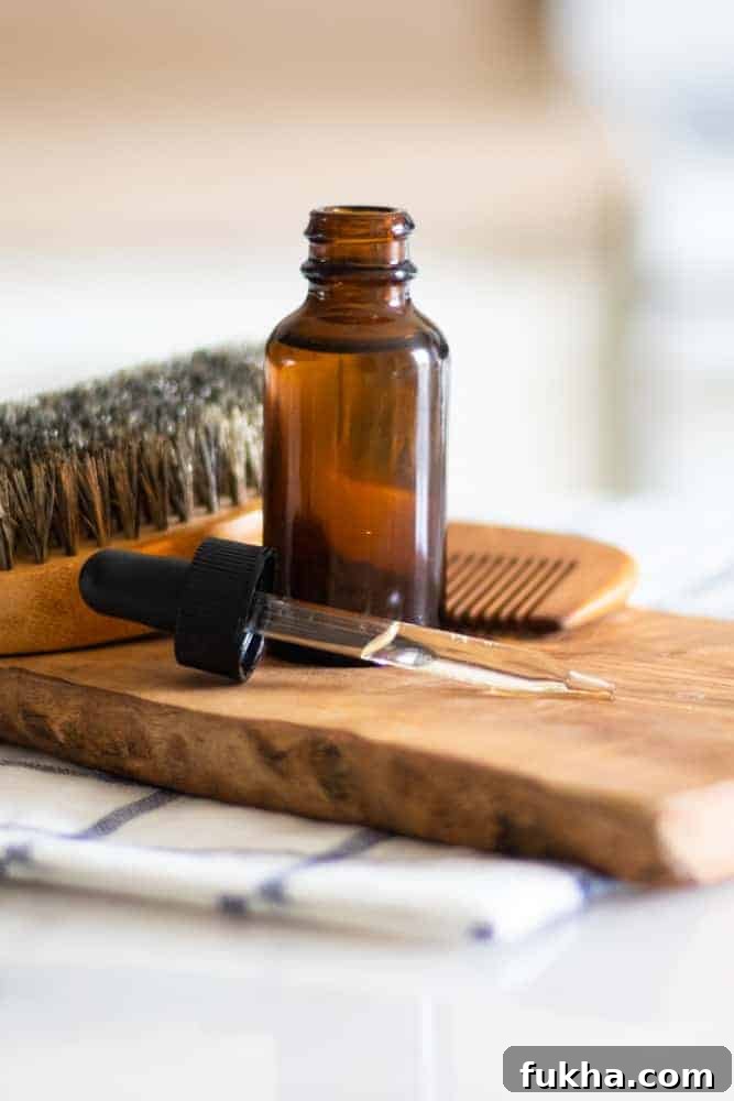 Dropper bottle with essential oils in it on wood board with bread brush and comb behind it.