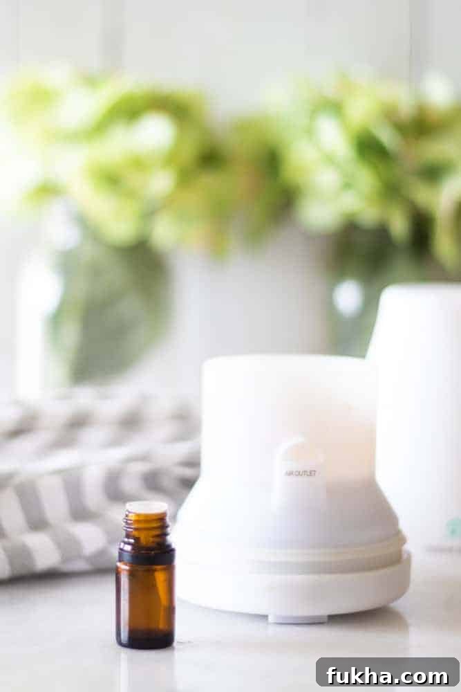 White diffuser on table with green flowers behind it.