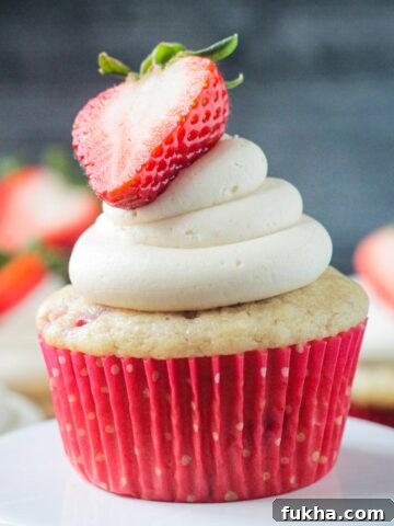 Close up of one vanilla frosted strawberry cupcake in a red paper liner.