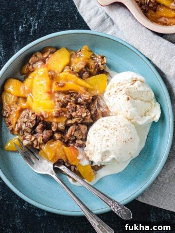 Vegan peach crisp with two scoops of vanilla ice cream on a blue plate.