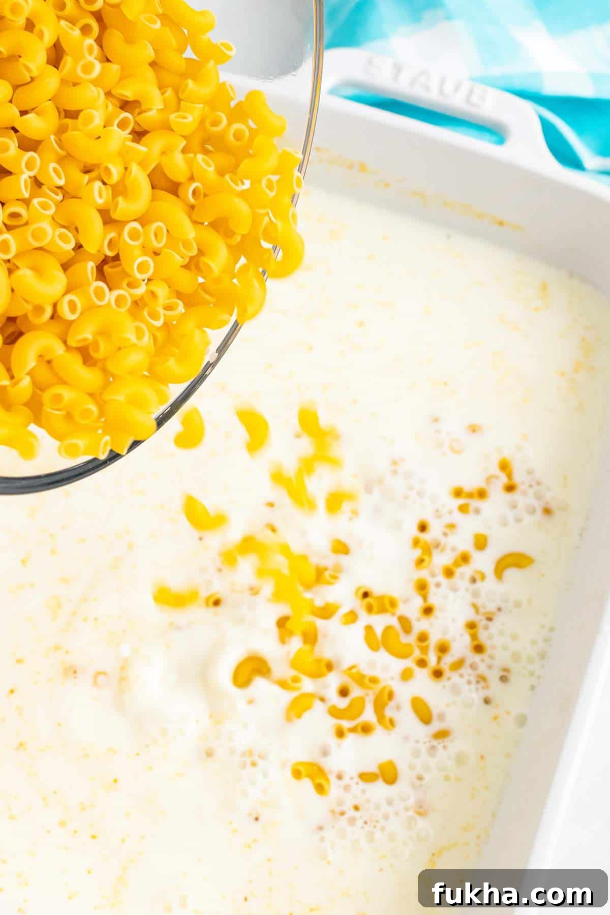 One-Pot No-Boil Mac and Cheese 5 Uncooked macaroni being poured into the milk mixture in the baking dish.