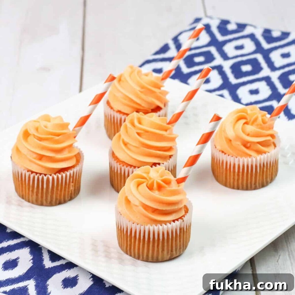 plate with orange cream soda cupcakes with a paper straw sticking out on side of frosting 