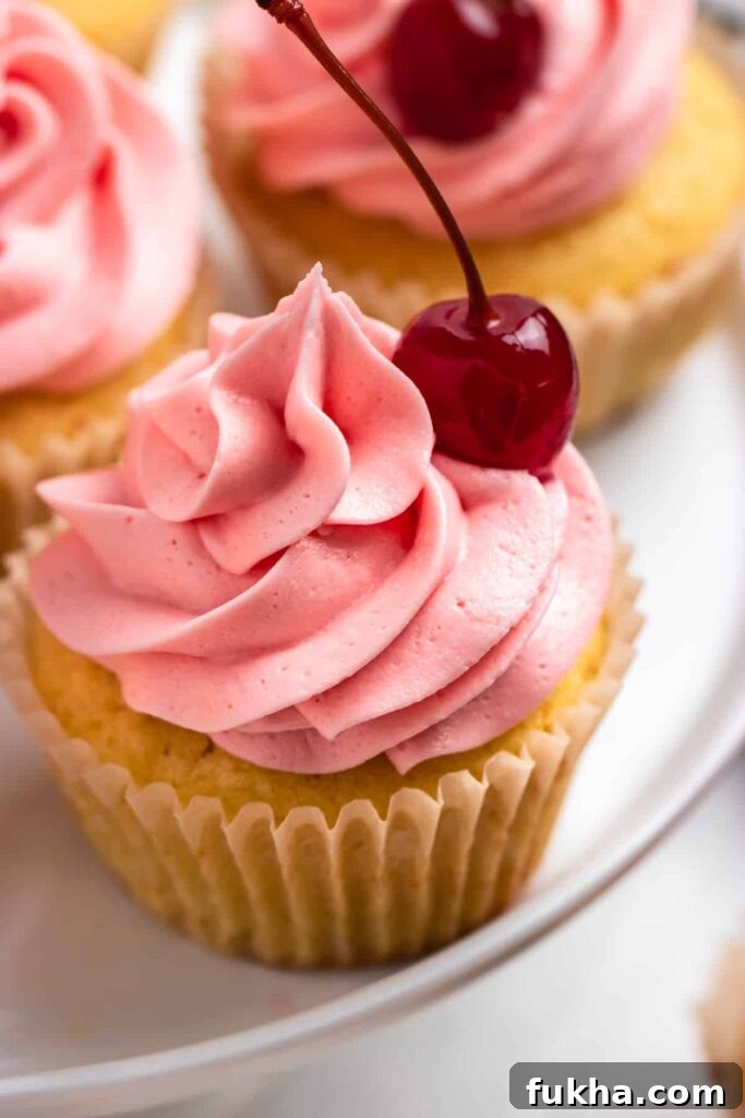 yellow colored cupcakes with pink frosting and a cherry sitting on the side of cupcake 