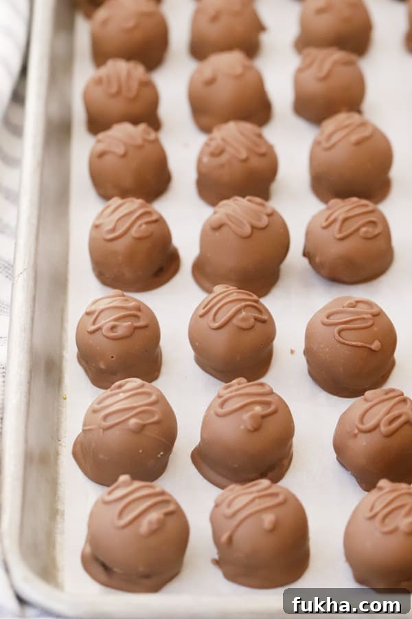 Chocolate-Covered Coconut Balls Recipe: Bite-Sized Truffles 4 Homemade coconut ball candy lined up on a sheet tray.