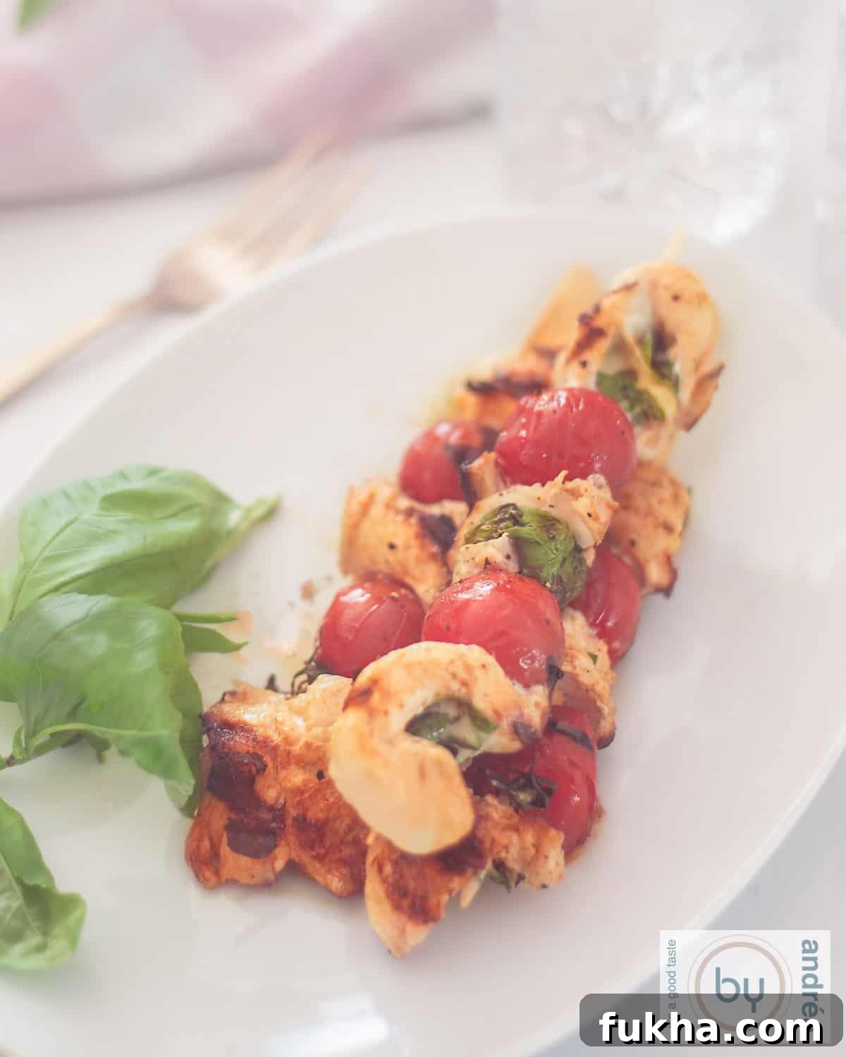 A top-down photo of a platter of three chicken skewers filled with mozzarella and basil with tomatoes.