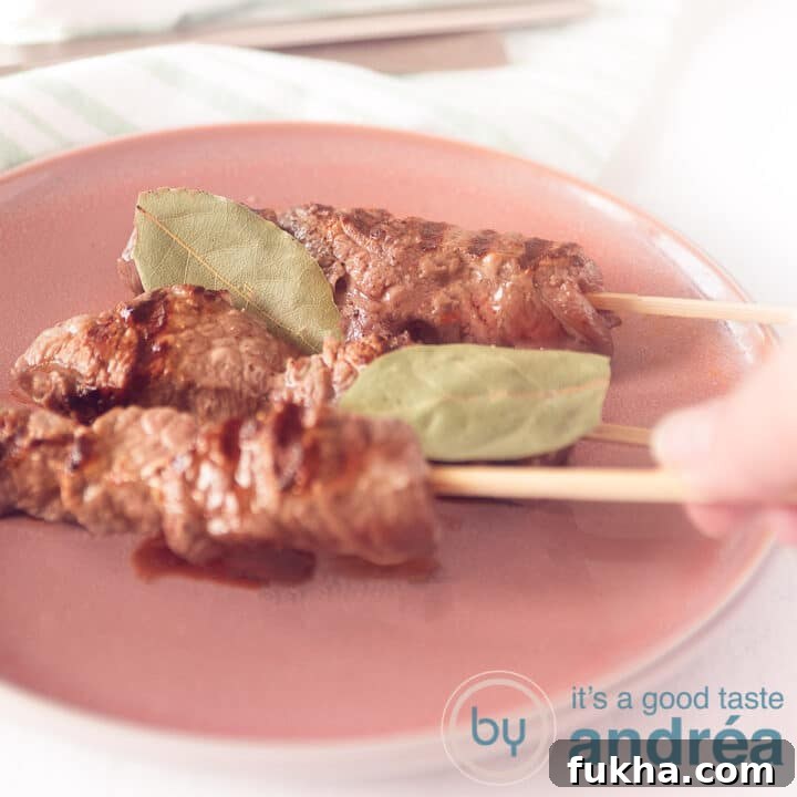 A square photo with a pink plate on which three Portuguese grilled skewers. A hand takes a skewer