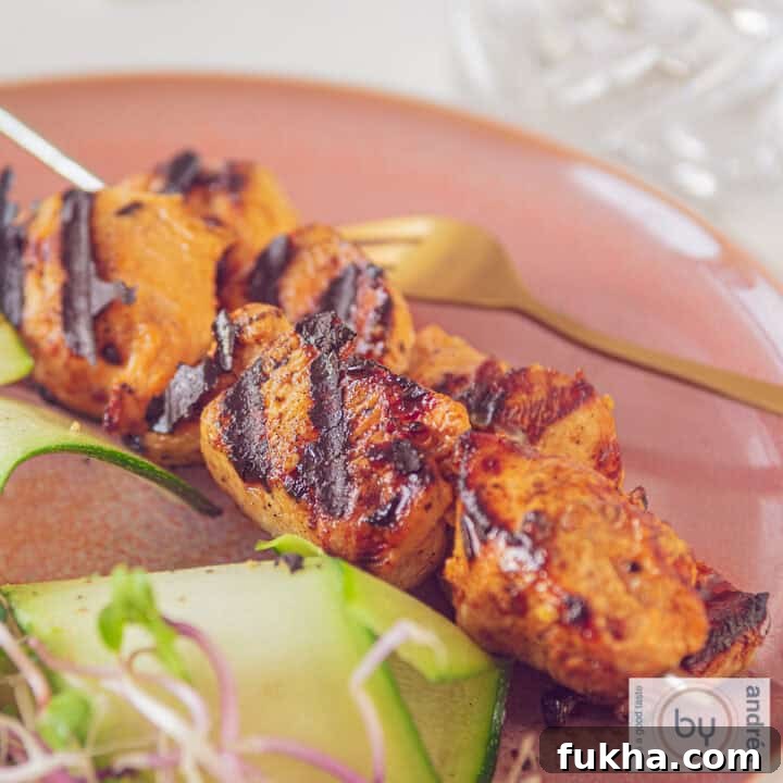 A square photo of two skewers on a red plate with chicken marinated in mustard and ketjap and grilled.