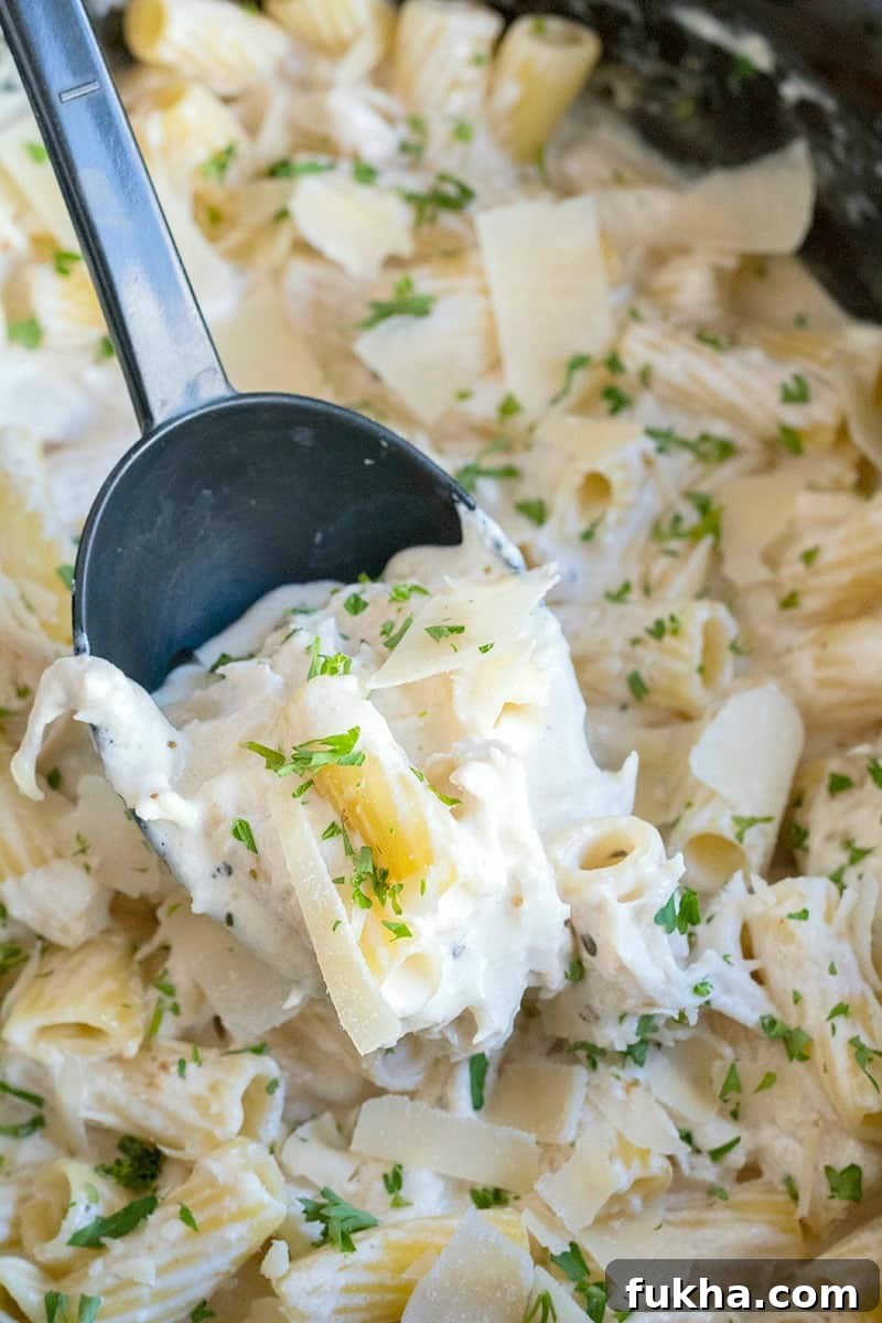 spoon lifting a serving of crock pot chicken alfredo out of the slow cooker