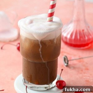 Cherry Americola: Cherry Coffee Drink Recipe 11 A cherry americola drink in a clear glass with a straw on a pink surface.