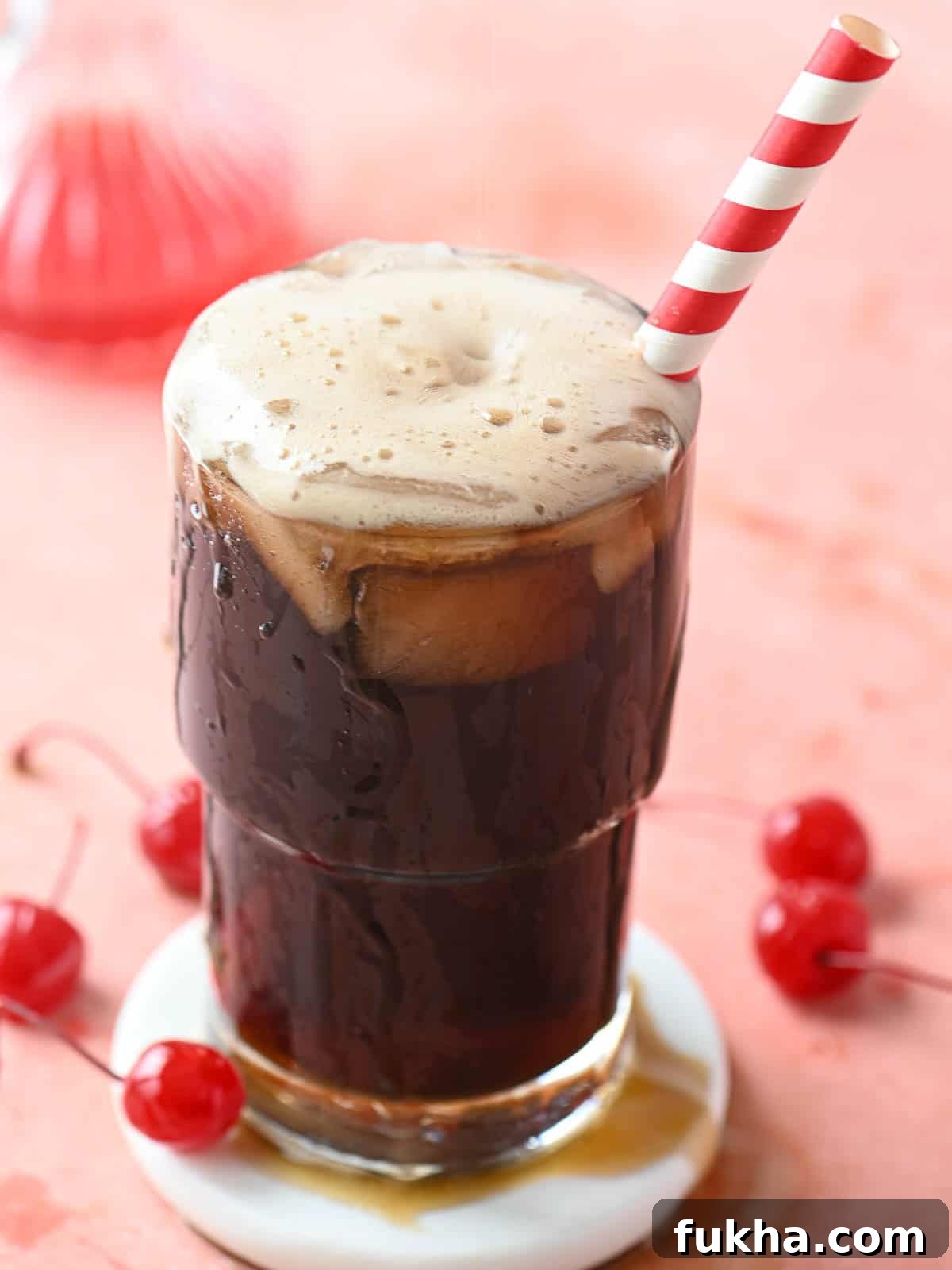 Cherry Americola: Cherry Coffee Drink Recipe 5 A cherry americola drink in a clear glass with a straw on a pink surface.