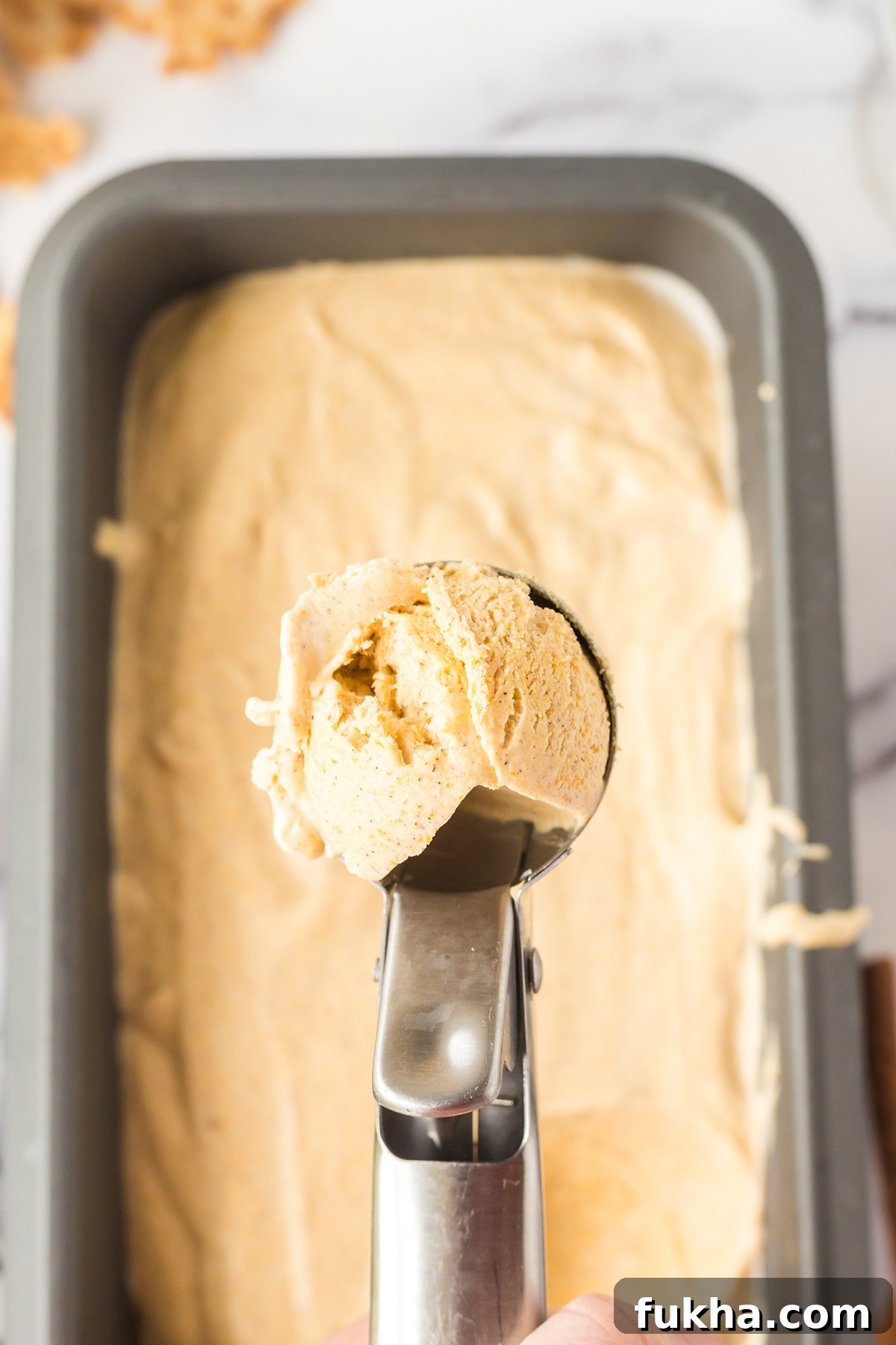 Scoop of pumpkin ice cream over frozen ice cream in loaf pan.