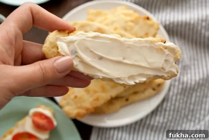 Hand holding a flatbread cracker covered in soft cheese