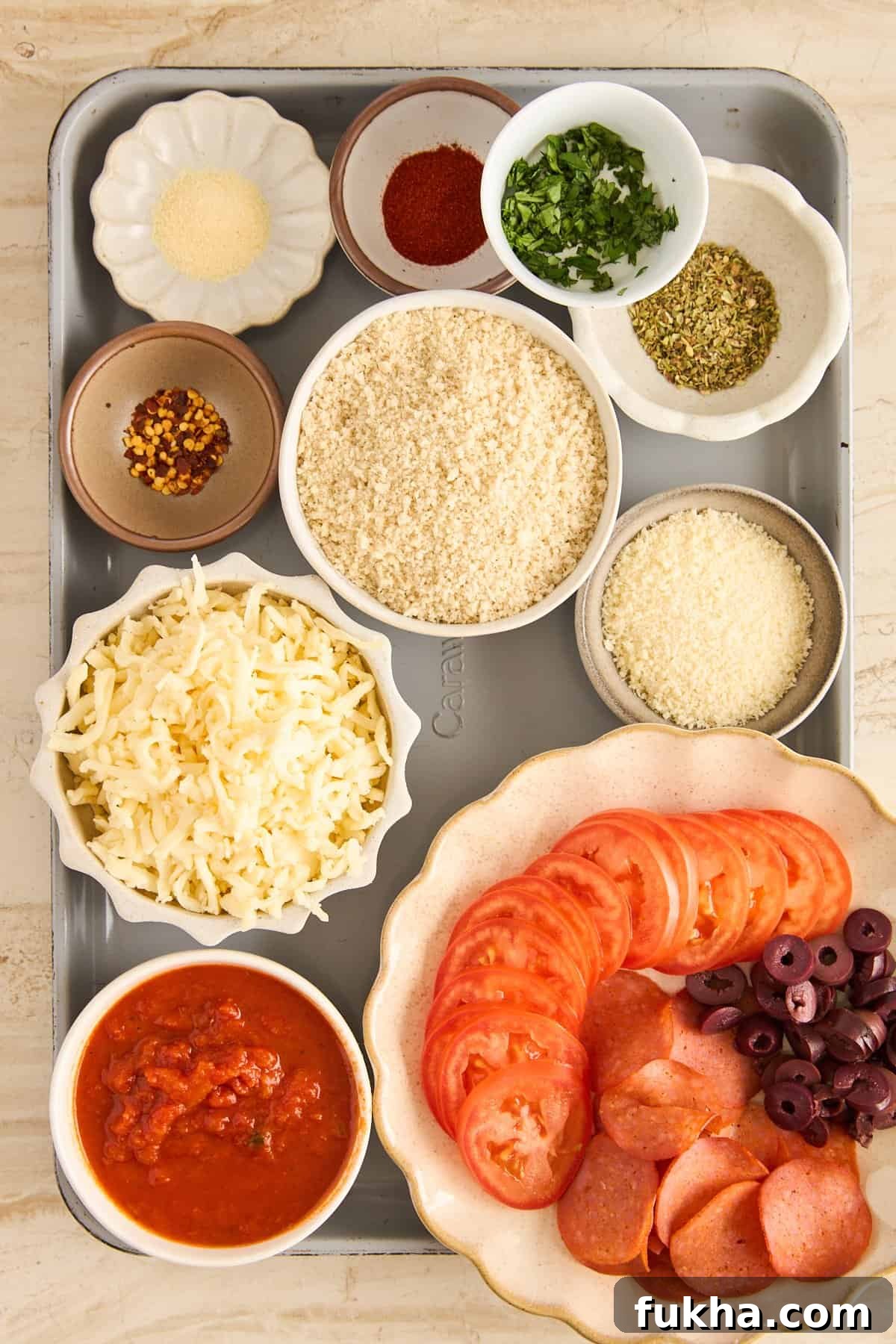 A tray with bowls of shredded cheese, tomato slices, sliced pepperoni, black olives, marinara sauce, breadcrumbs, grated parmesan, and small bowls of various spices and herbs.