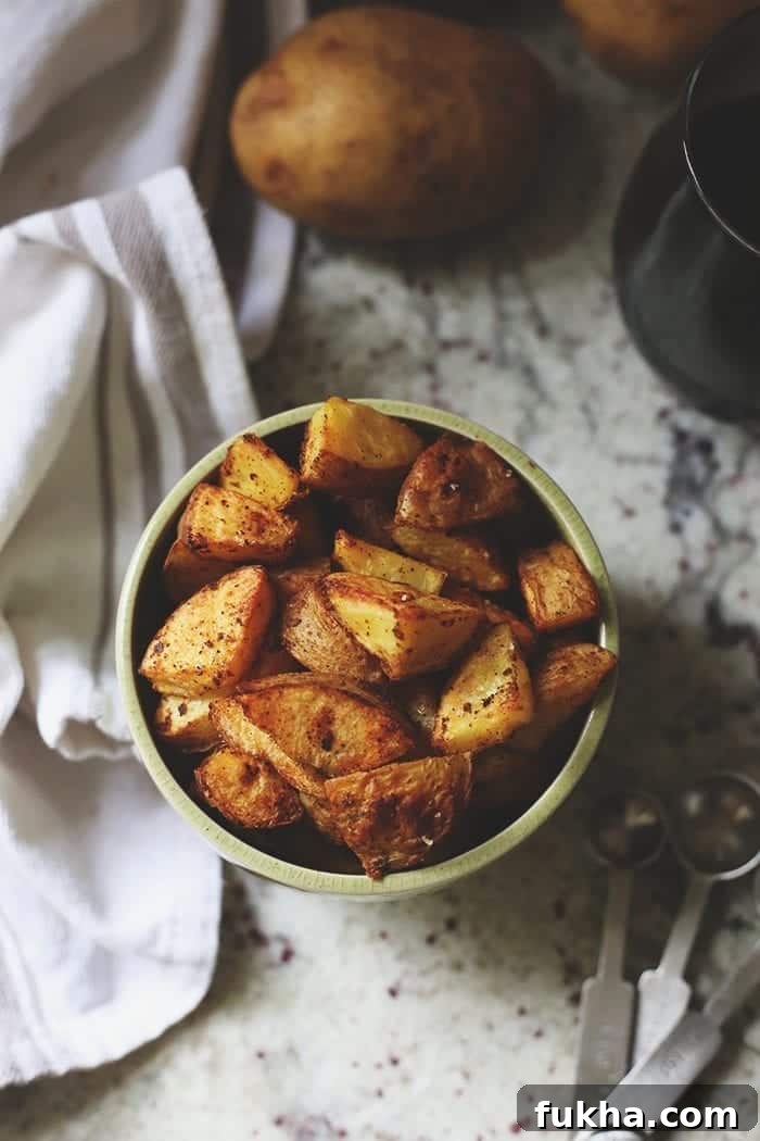 Crispy Roasted Potatoes: Oven and Air Fryer Methods 10 Overhead image of roasted potatoes in a green bowl topped with spices.