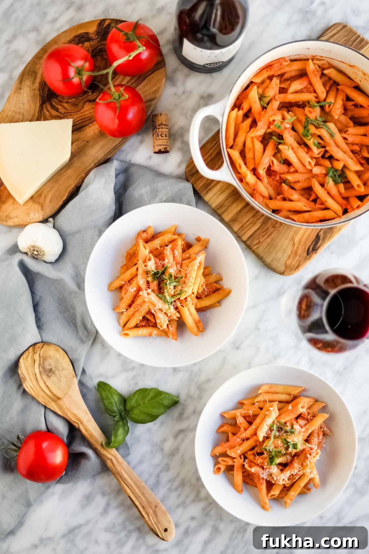 Penne pasta with vodka sauce in white bowls and dutch oven with wine, basil, garlic, tomatoes and cheese.