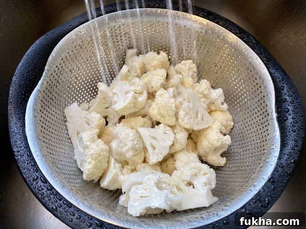 Vegan Roasted Curried Cauliflower with Coconut and Turmeric 3 I am rinsing cauliflower florets in a colander in the sink.