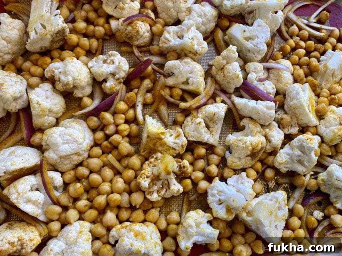 Vegan Roasted Curried Cauliflower with Coconut and Turmeric 4 Seasoned cauliflower, chickpeas, and red onions on a baking sheet.