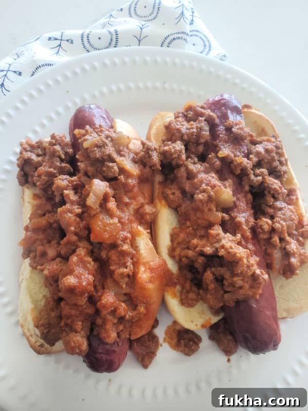 two chili dogs with homemade hot dog chili over them on a white plate
