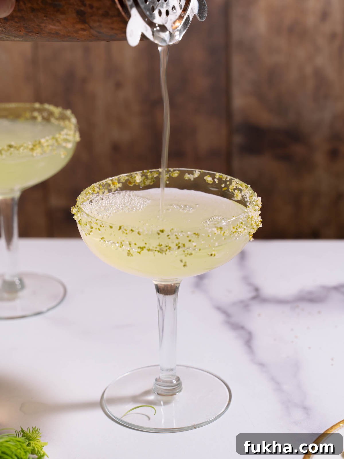 Pouring fir tip lemon drop cocktail mixture into a coupe glass