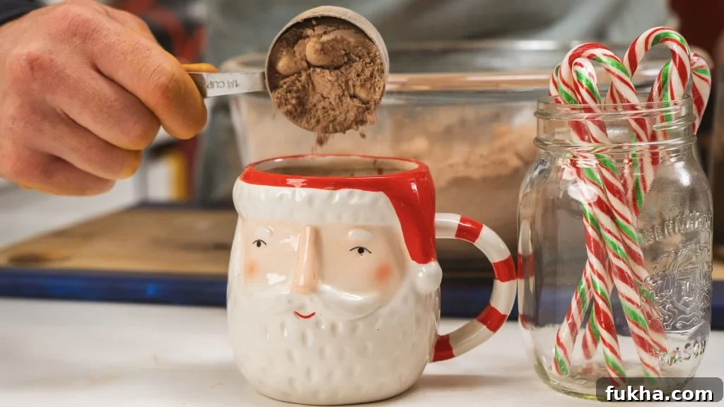 Homemade Hot Chocolate Mix Recipe for Holiday Gifts 3 A Santa mug being filled with a scoop of homemade hot chocolate mix. Visible in the front is a candy cane and a jar of candy canes to the right.
