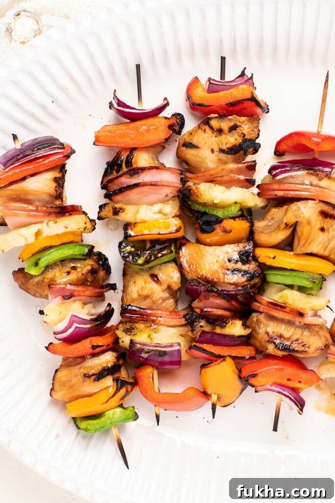 A close up look at 4 chicken skewers with purple onion and colorful bell peppers.