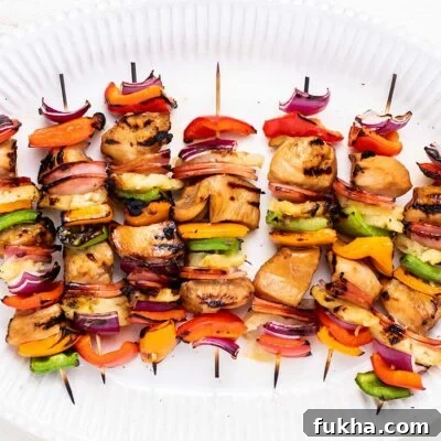 A white platter with colorful grilled teriyaki chicken skewers.