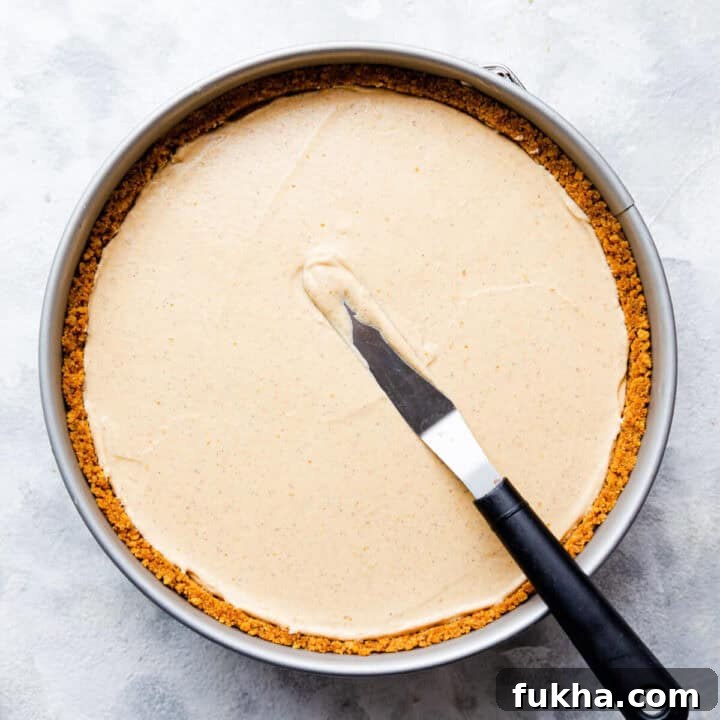 top view of a round baking tin with pumpkin cheesecake inside and small offset spatula on top