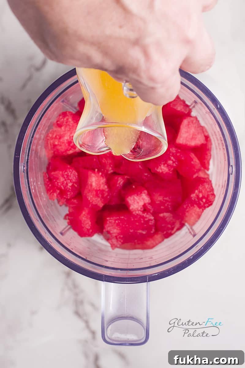 a hand pouring orange juice into a blender jar with watermelon