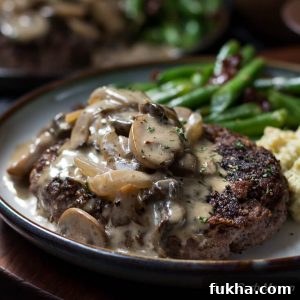 Hamburger steak and gravy of mushrooms and onions on a plate with green beans with bacon and cheesy mashed cauliflower.