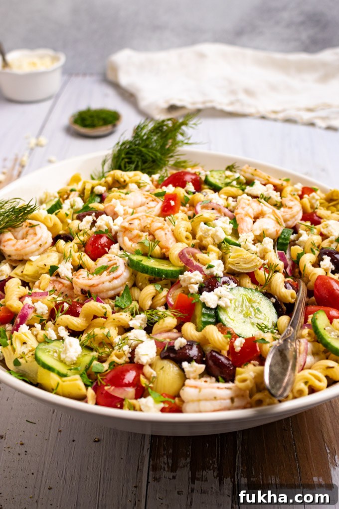 Angled shot of Greek Pasta salad in a large serving bowl on a rustic white wood background.