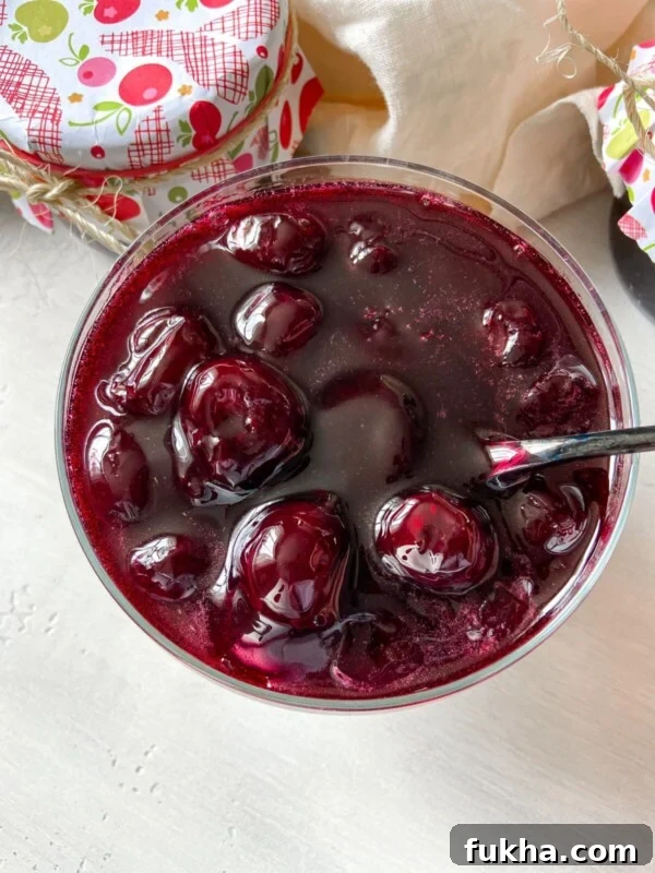 A close-up of a glass bowl filled with cherry preserves featuring whole cherries in glossy syrup.