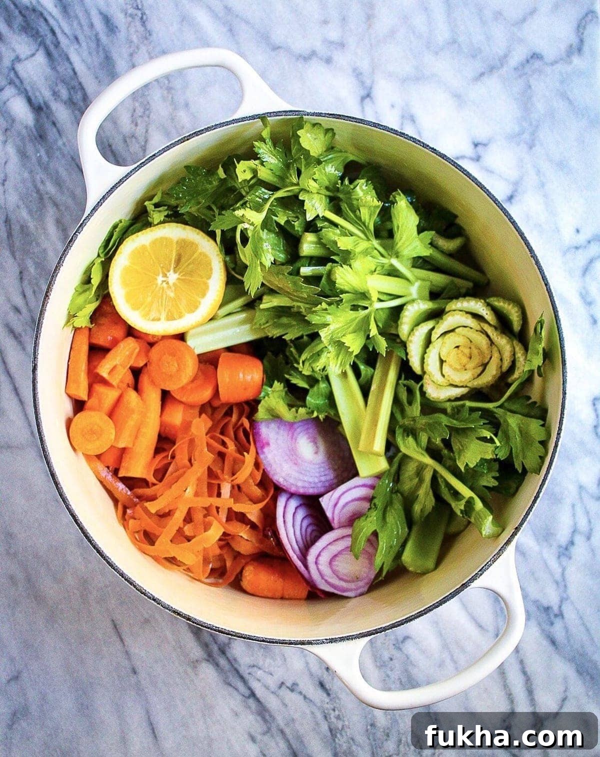 A white pot filled with celery, carrots, onion, and lemon