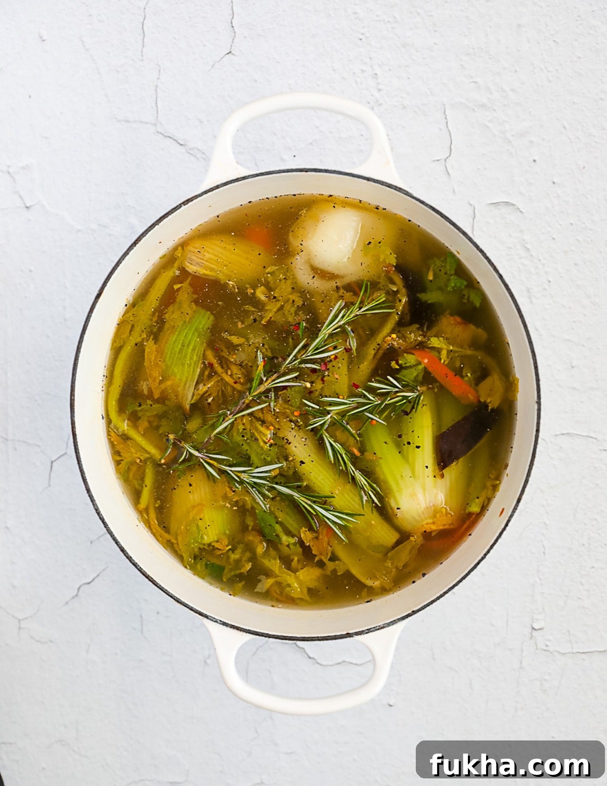 A white pot filled with vegetables, fresh herbs, and water.