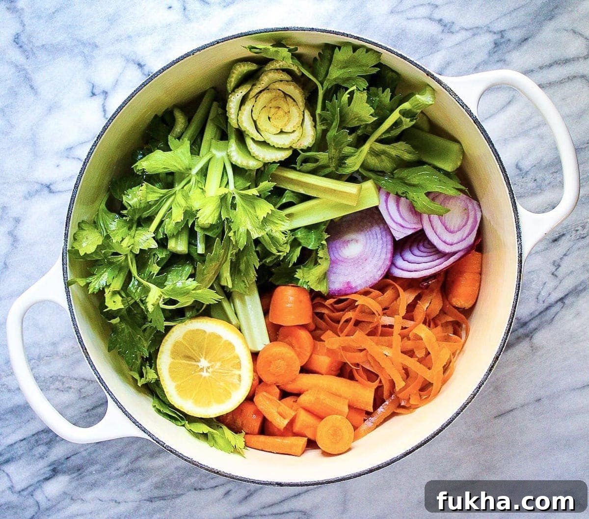 A large white pot filled with celery, lemon, carrots, and onion