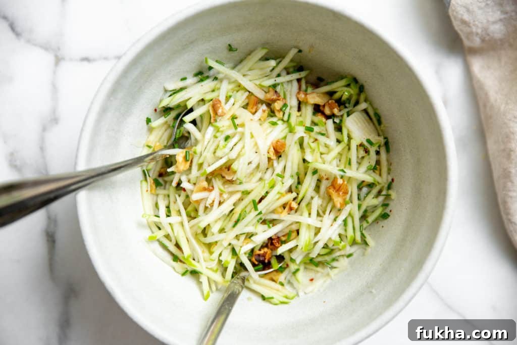 Apple slaw in a serving bowl with serving spoons.