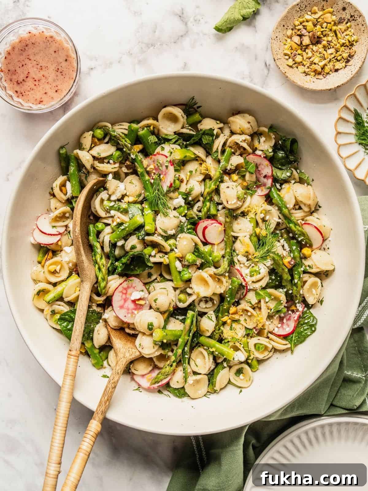 Bowl of spring pasta salad loaded with asparagus, radish, spinach, herbs and a tangy sumac honey dressing.