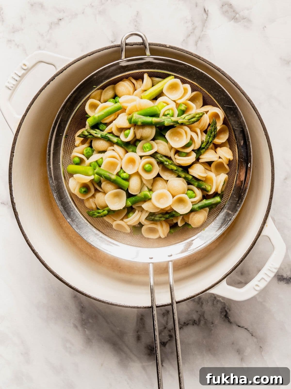 A colander draining pasta, peas and asparagus.