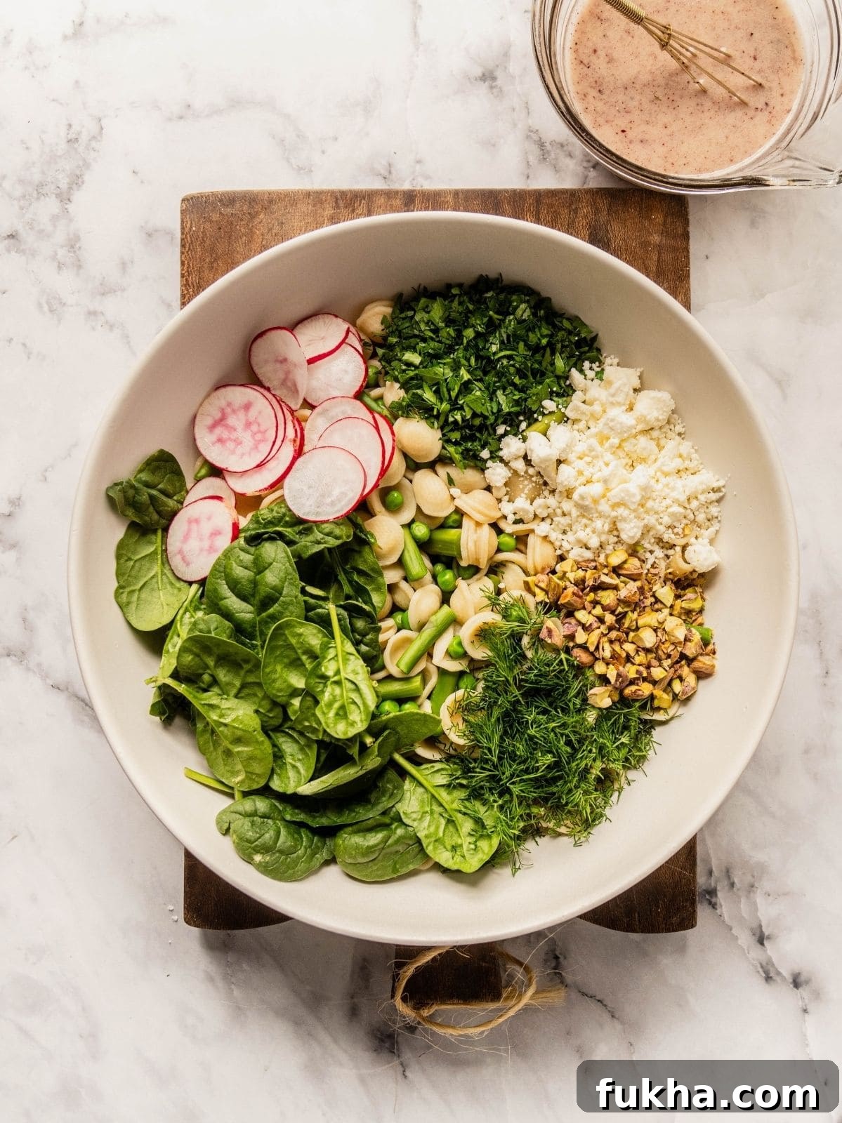 Bowl with cooked pasta, vegetables, herbs, cheese and pistachios.