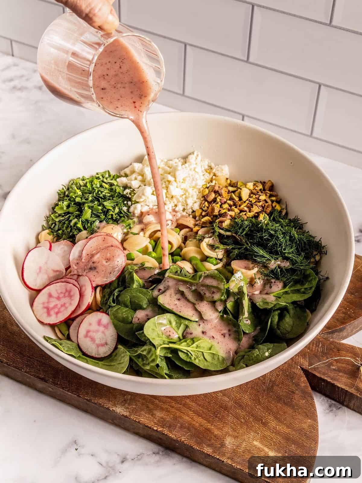 Pouring the sumac honey lemon dressing over the pasta salad ingredients.