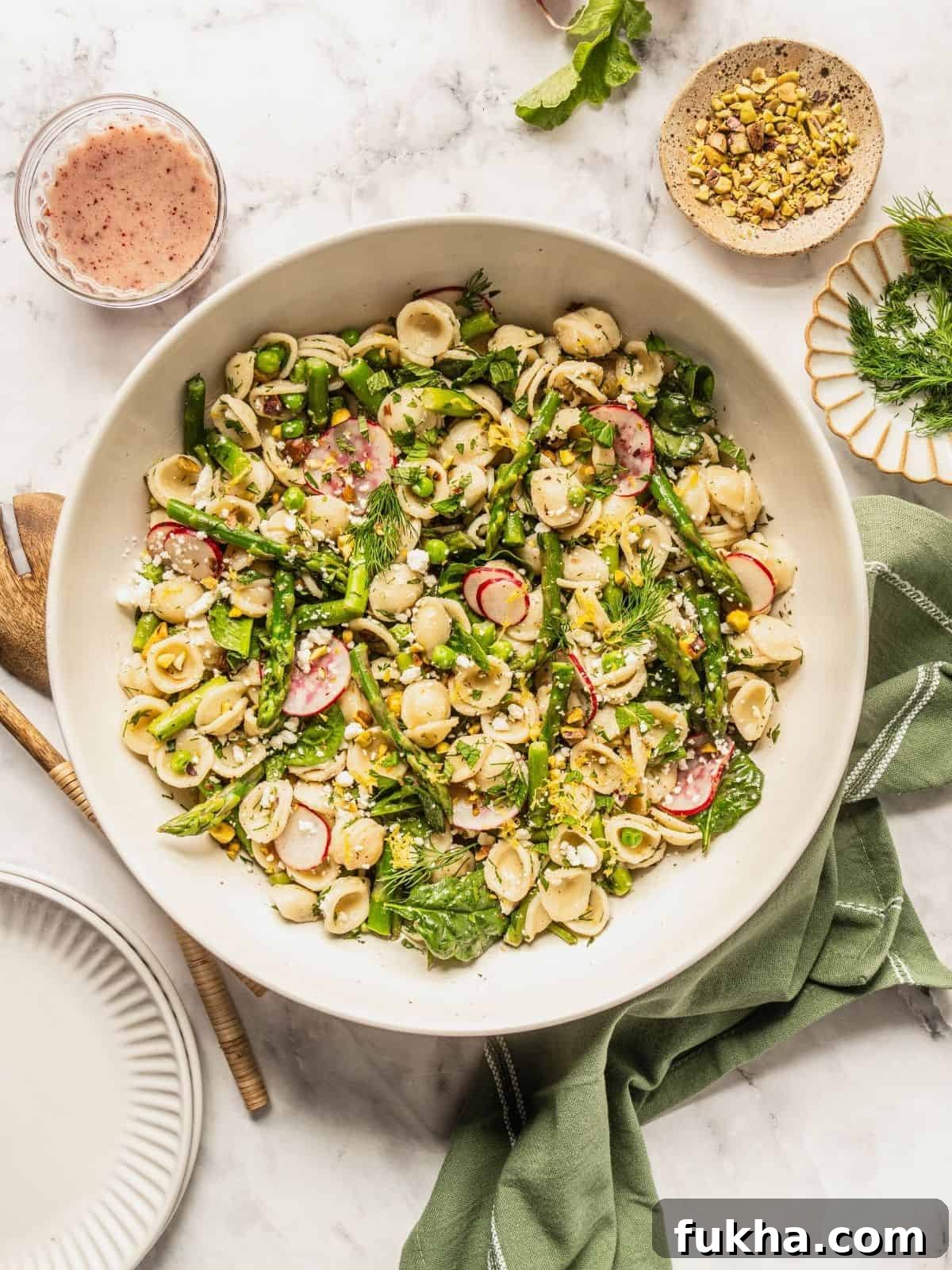 Bowl of spring pasta salad loaded with asparagus, radish, spinach, herbs and sumac honey dressing.