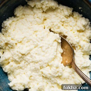 Homemade ricotta cheese in a blue bowl with a spoon.