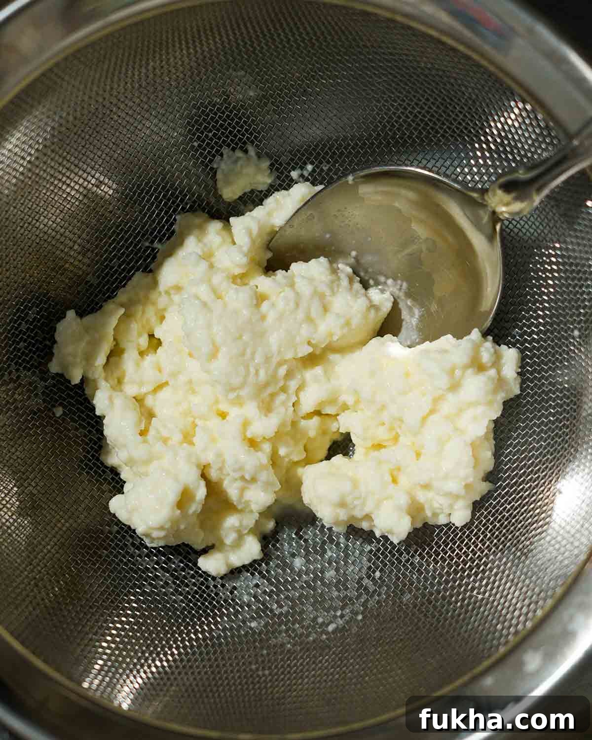 Homemade ricotta being strained out over a fine mesh sieve.