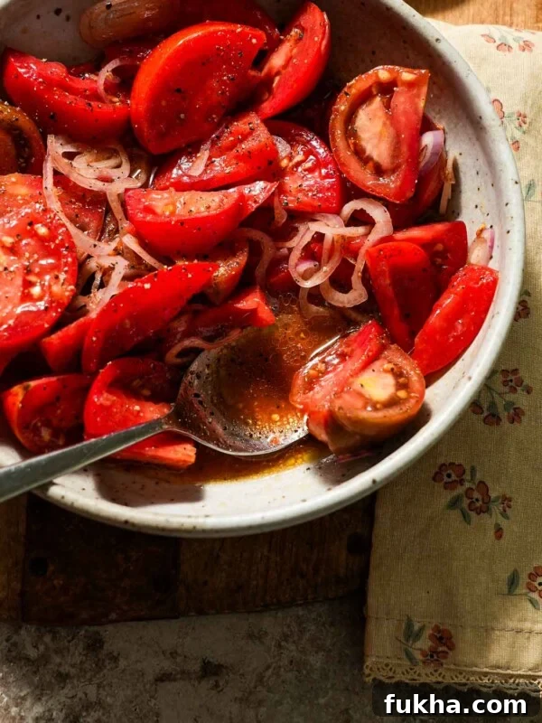 A bowl of marinated tomatoes with a spoon of juices.